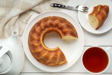 Photo of Delicious homemade yogurt cake and cup tea on white wooden table, flat lay