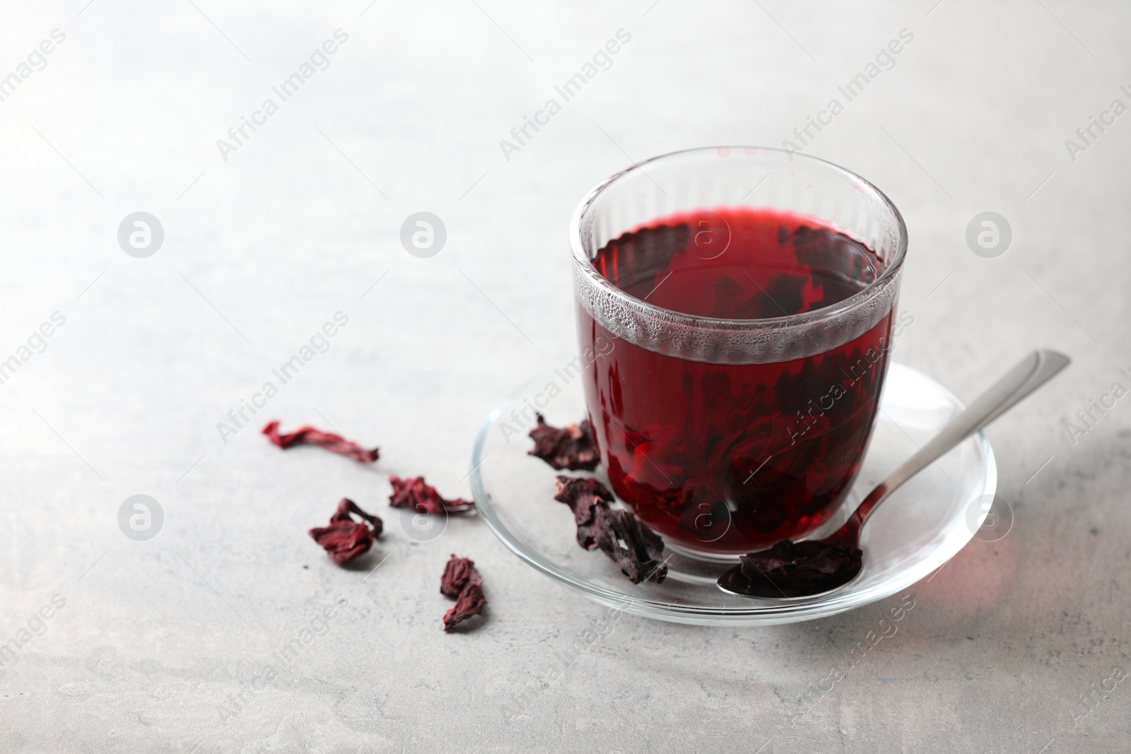 Photo of Aromatic hibiscus tea in glass, dried roselle calyces and spoon on light table, space for text