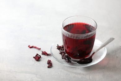Aromatic hibiscus tea in glass, dried roselle calyces and spoon on light table, space for text