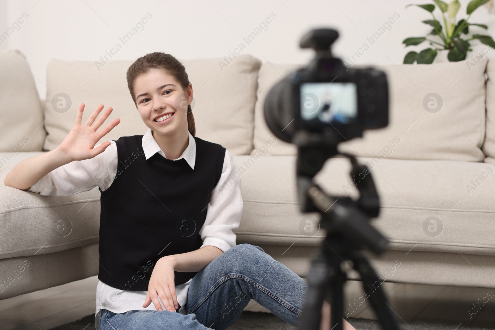 Photo of Smiling teenage blogger waving hello to her subscribers while streaming at home