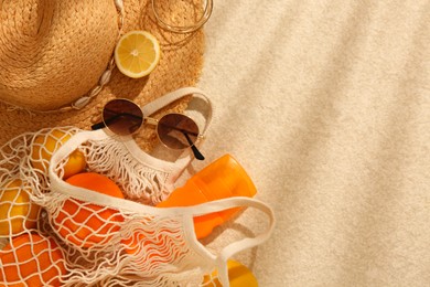 Photo of String bag with sunglasses, straw hat and fruits on beige textured background, flat lay. Space for text