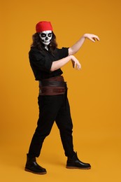 Photo of Man in scary pirate costume with skull makeup posing on orange background. Halloween celebration