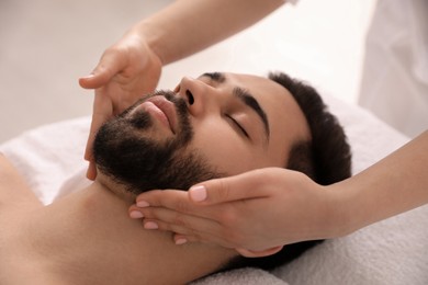 Photo of Young man receiving facial massage in beauty salon, closeup