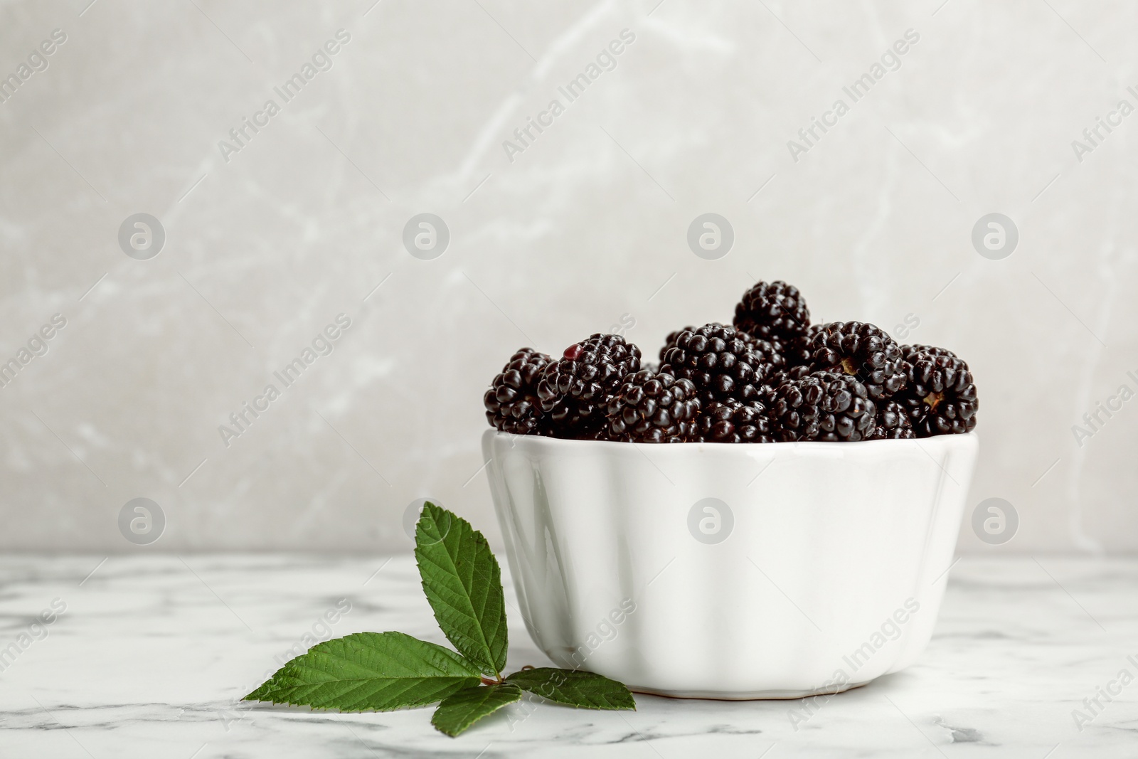 Photo of Bowl of fresh blackberry on marble table. Space for text