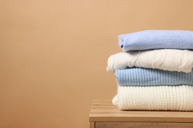 Stack of casual sweaters on wooden table against light brown background. Space for text