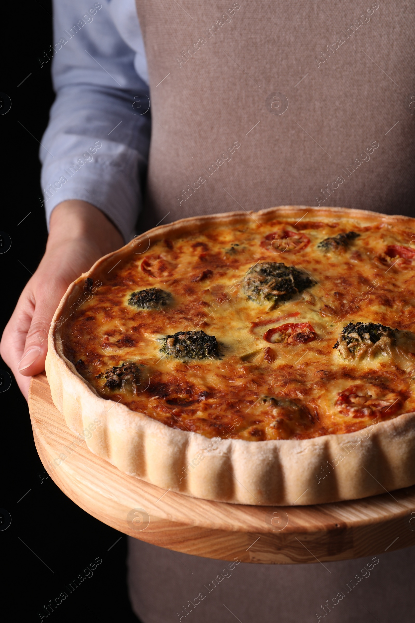 Photo of Woman holding delicious homemade vegetable quiche on black background, closeup