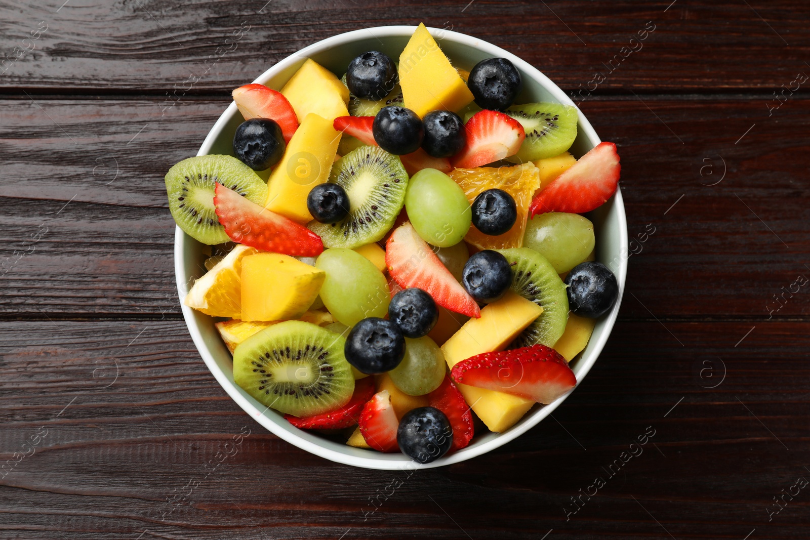 Photo of Tasty fruit salad in bowl on wooden table, top view