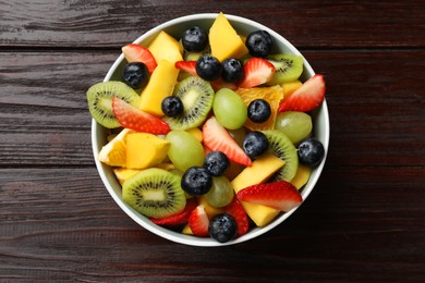 Tasty fruit salad in bowl on wooden table, top view