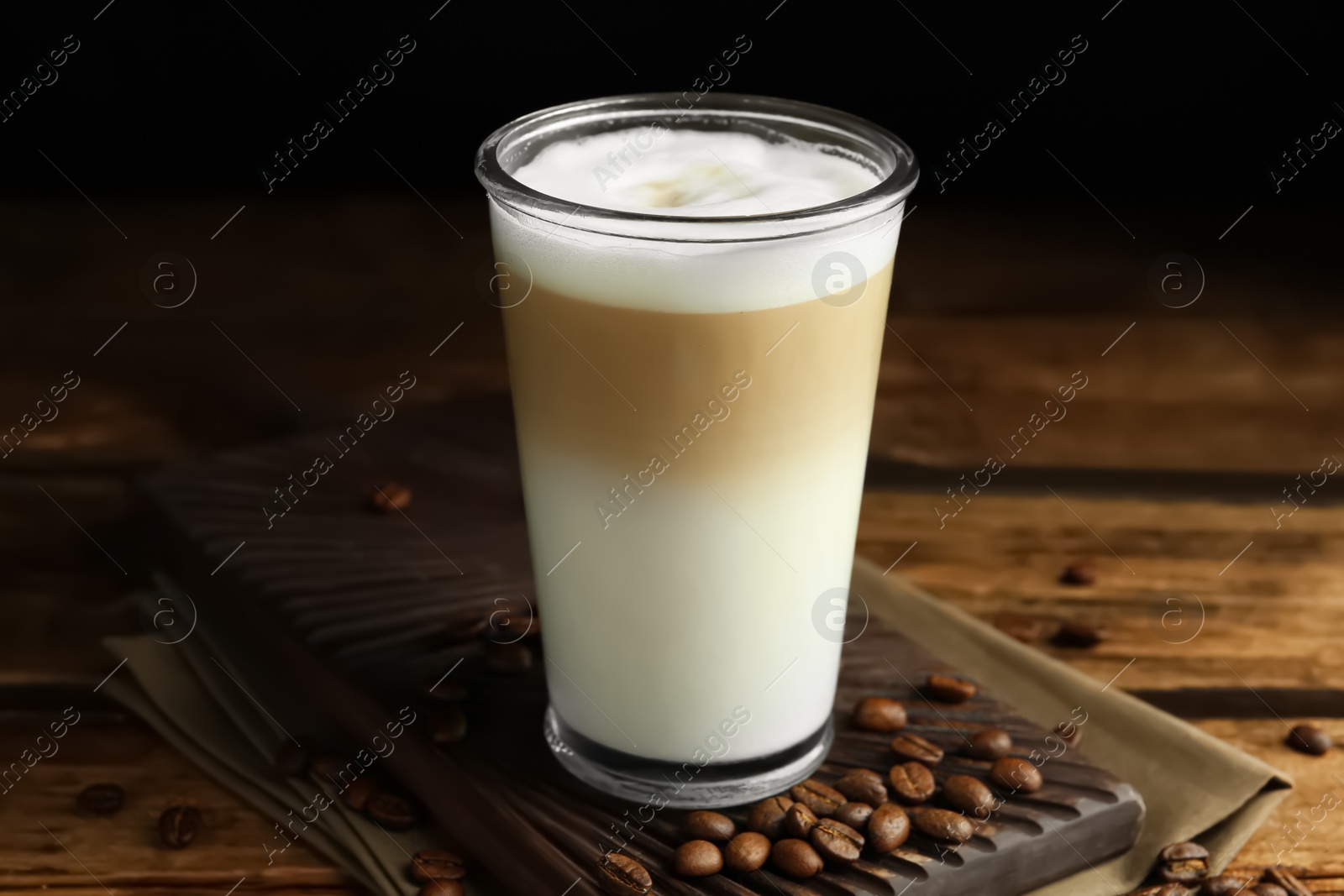 Photo of Delicious latte macchiato and coffee beans on wooden table