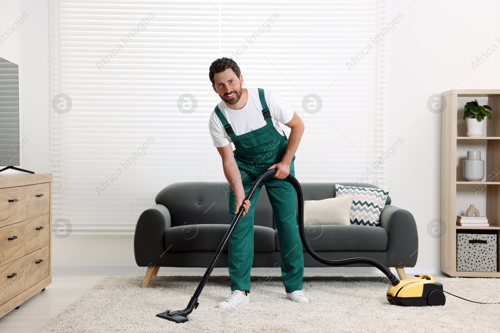 Photo of Dry cleaner's employee hoovering carpet with vacuum cleaner in room