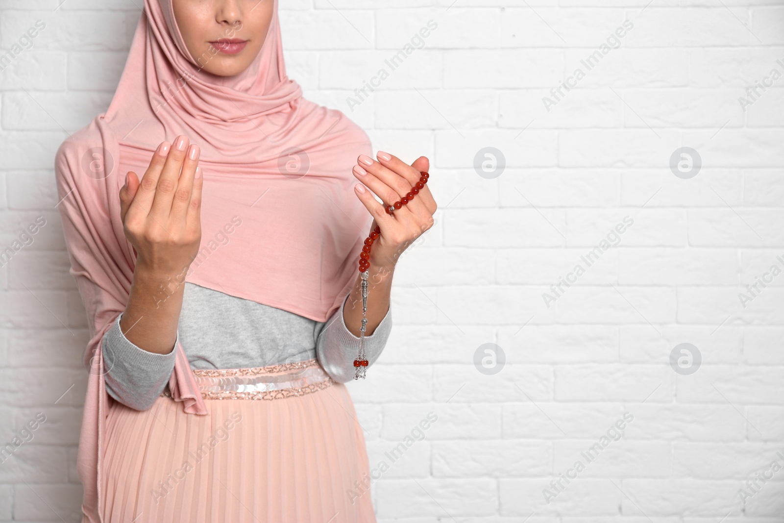 Photo of Young Muslim woman praying against brick wall, closeup. Space for text