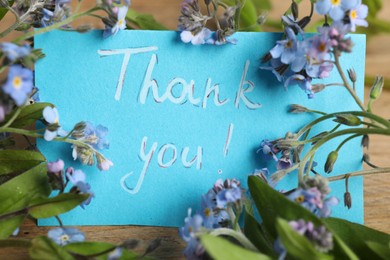 Photo of Card with phrase Thank You and beautiful forget-me-not flowers on table, closeup