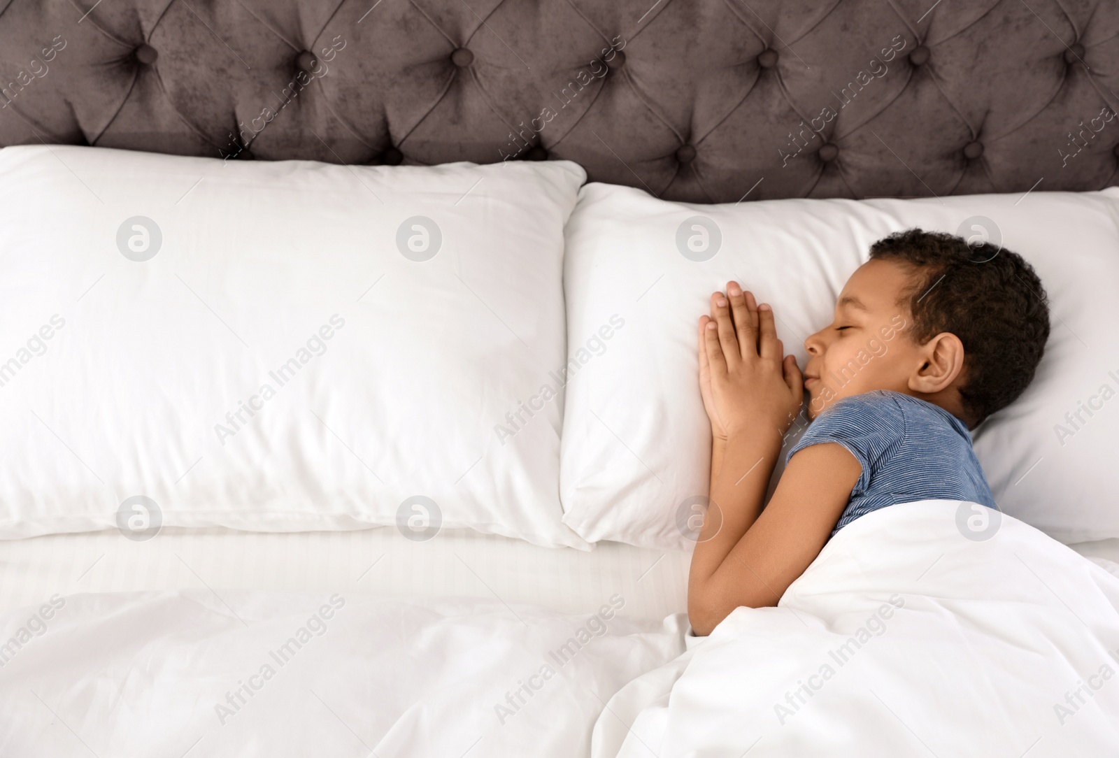 Photo of Cute little African-American boy sleeping in bed, above view