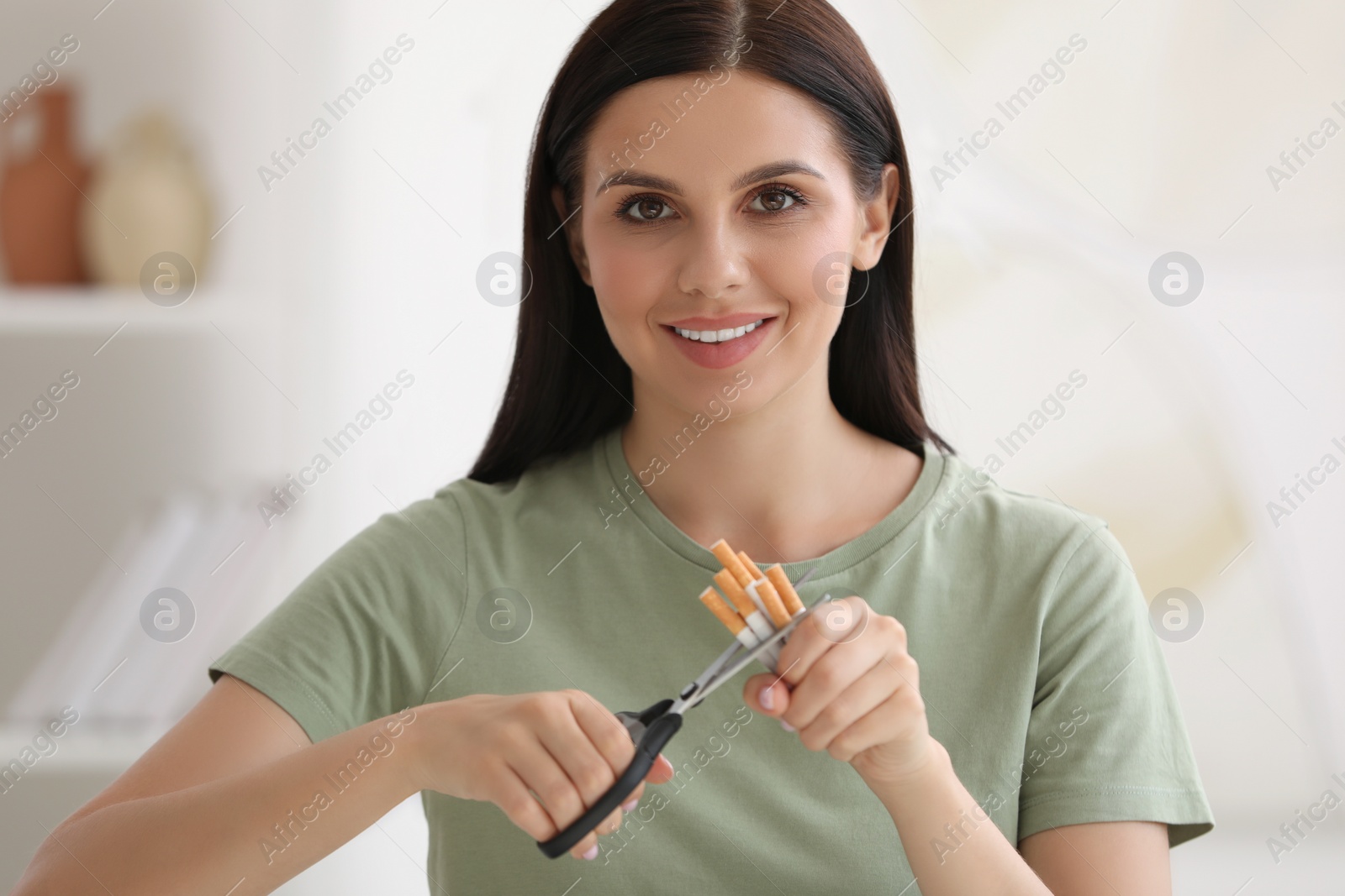 Photo of Stop smoking concept. Young woman cutting cigarettes on blurred background