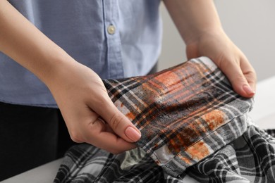 Woman showing stain from sauce on shirt at table against blurred background, closeup