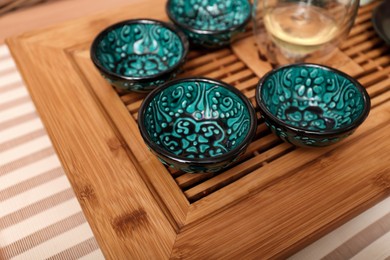 Wooden tray with cups for traditional tea ceremony on pink fabric, closeup