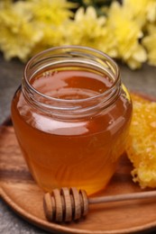 Sweet golden honey in jar and dipper on grey table, closeup