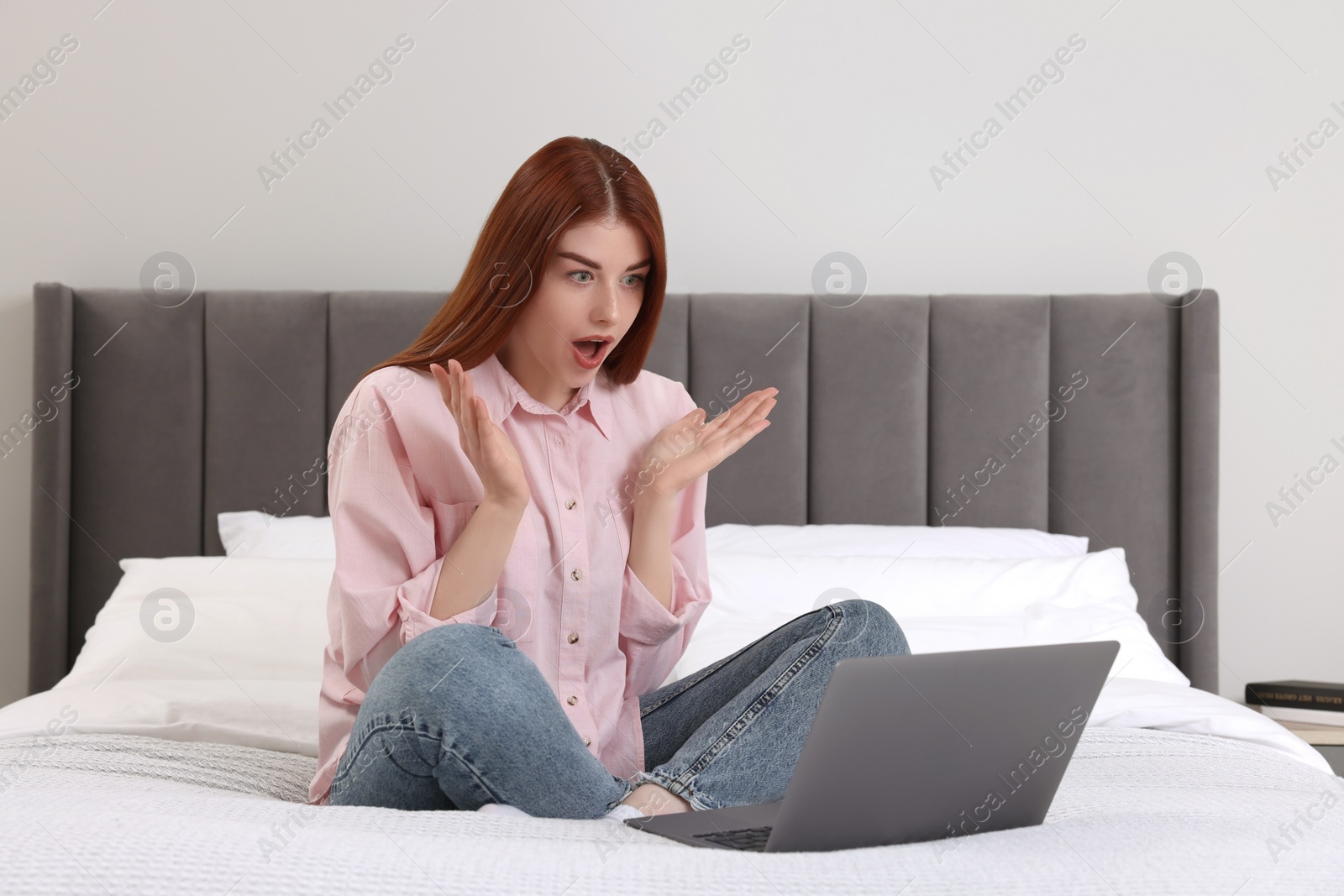 Photo of Shocked woman with laptop on bed in bedroom