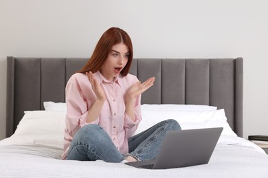 Shocked woman with laptop on bed in bedroom