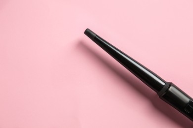 Photo of Modern clipless curling hair iron on pink background, top view. Space for text