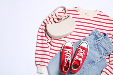 Photo of New stylish red sneakers, jeans, striped sweater and bag on white background, flat lay and space for text. Casual outfit