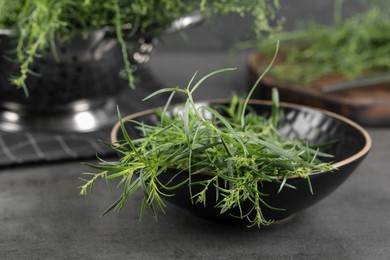 Photo of Fresh tarragon sprigs in bowl on grey table