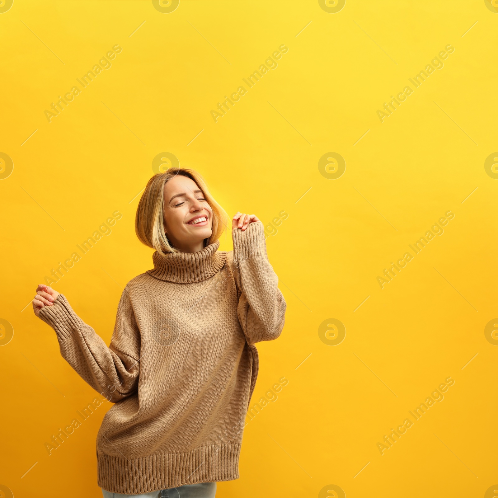 Photo of Beautiful young woman wearing knitted sweater on yellow background. Space for text