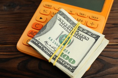 Photo of Money exchange. Dollar banknotes and calculator on wooden background, closeup