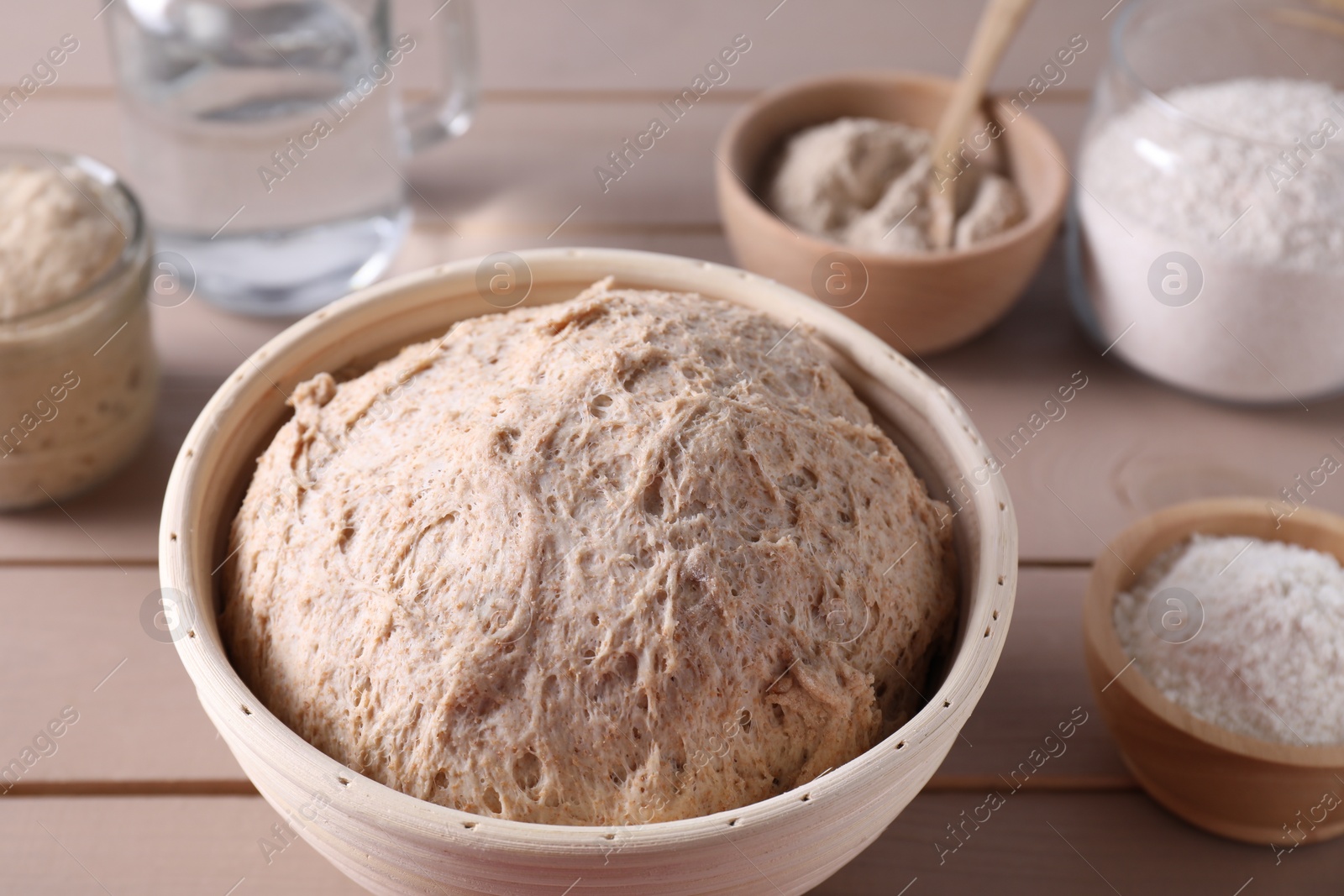 Photo of Fresh sourdough in proofing basket and flour on wooden table, closeup