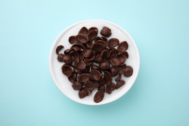 Photo of Breakfast cereal. Chocolate corn flakes and milk in bowl on turquoise background, top view