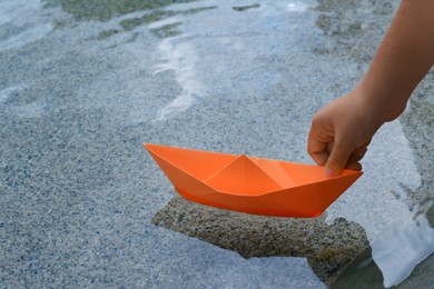 Photo of Kid launching small orange paper boat on water outdoors, closeup