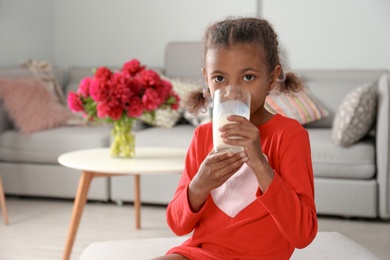 Adorable African-American girl with glass of milk at home