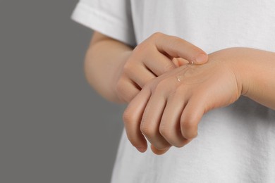 Child applying ointment onto hand against grey background, closeup. Space for text