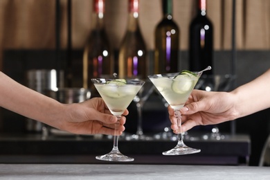 Young people clinking glasses of tasty cucumber martini at bar counter, closeup