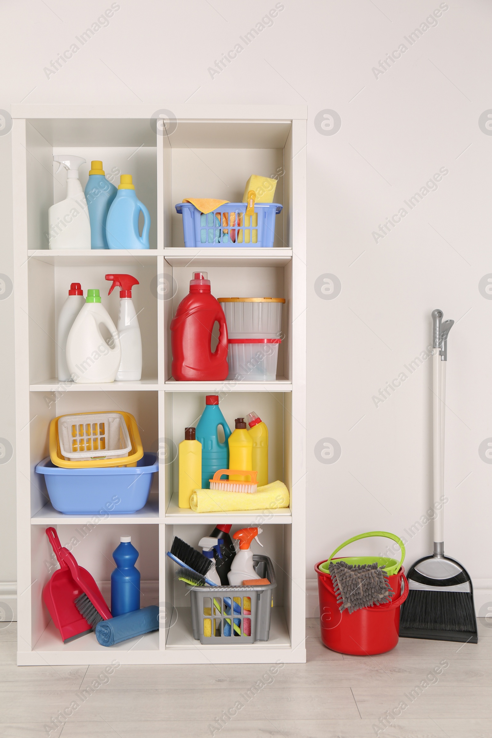 Photo of Shelving unit with detergents and cleaning tools near white wall indoors