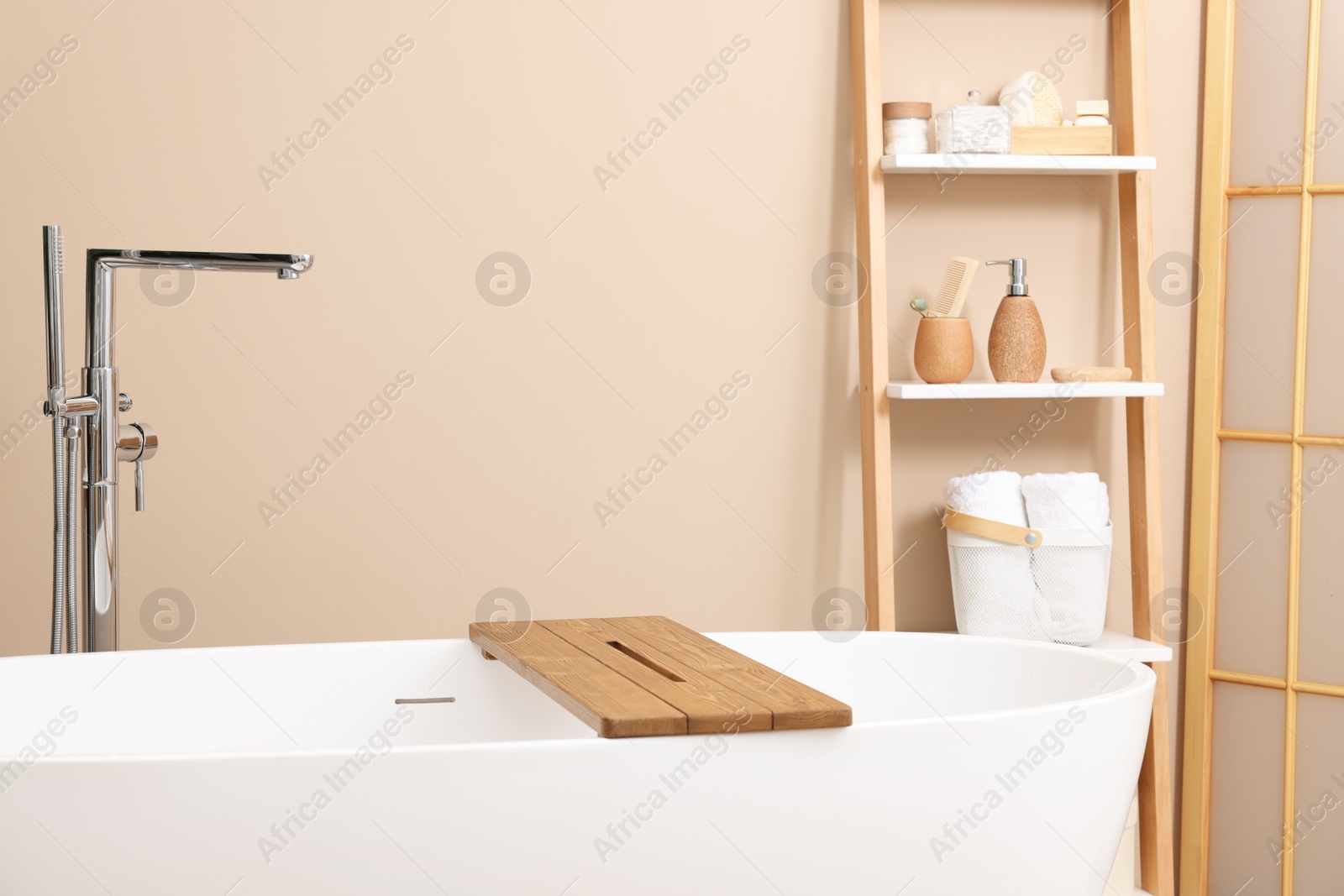 Photo of Bath tub with wooden board and different personal care products and accessories on shelving unit in bathroom