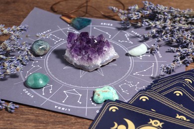 Photo of Astrology prediction. Zodiac wheel, gemstones, tarot cards and lavender on wooden table, closeup