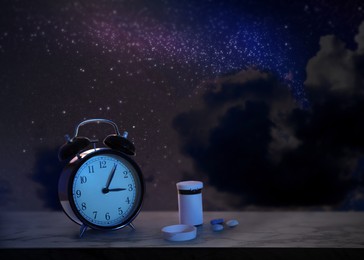 Image of Alarm clock and soporific pills on grey table against night sky with stars. Insomnia