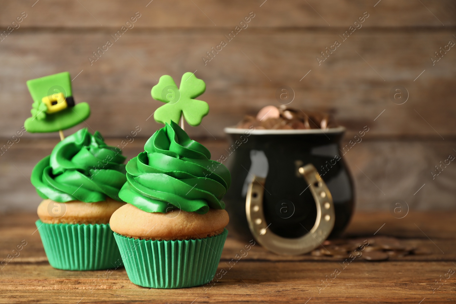 Photo of Decorated cupcakes and pot with gold coins on wooden table. St. Patrick's Day celebration