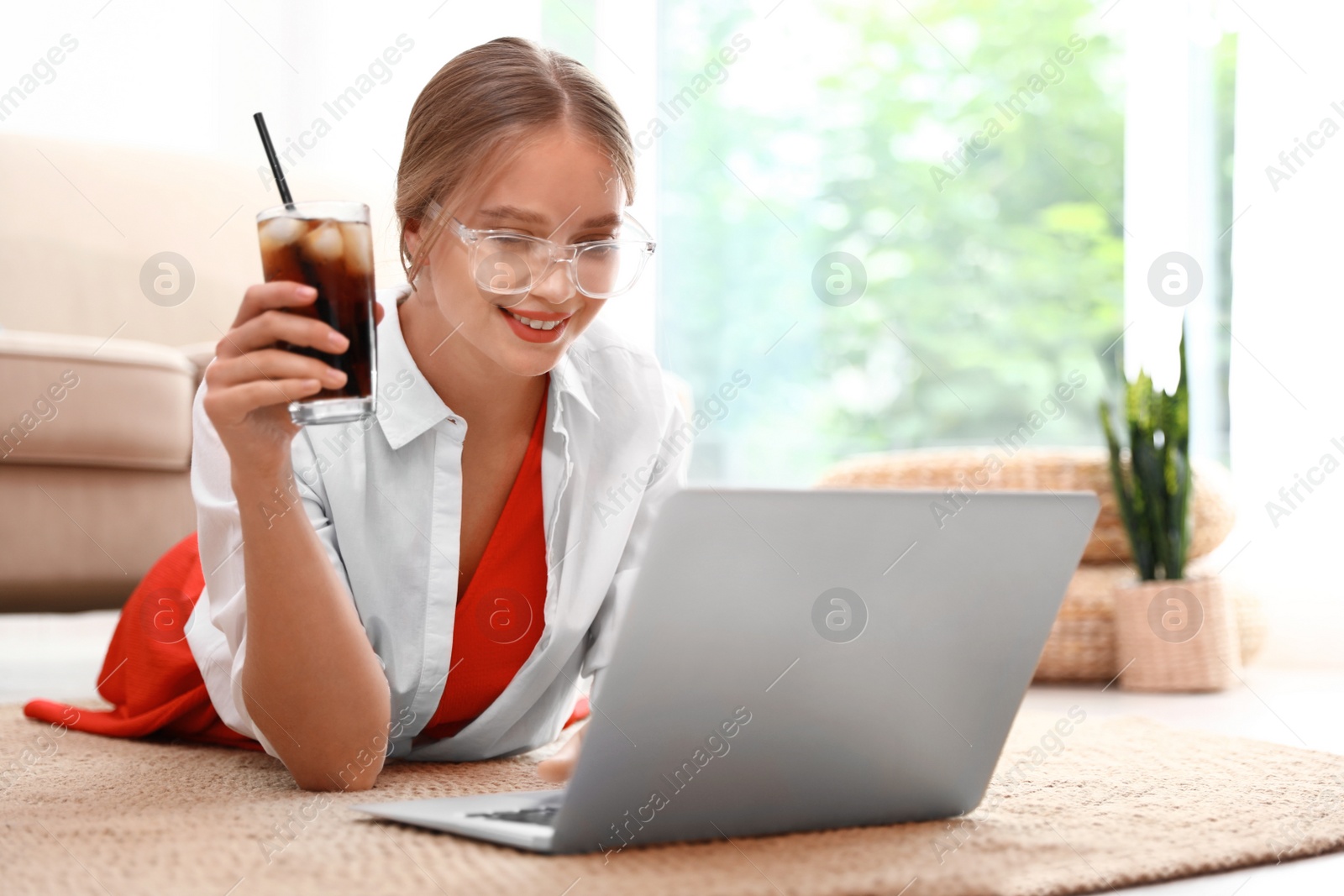 Photo of Young woman with glass of cola working on laptop at home. Refreshing drink