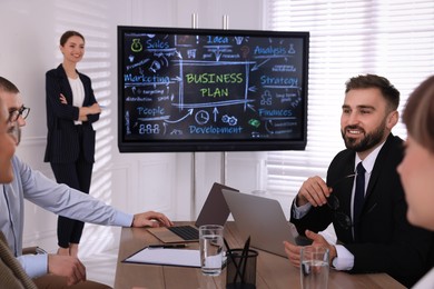 Business trainer near interactive board in meeting room during presentation, focus on colleagues