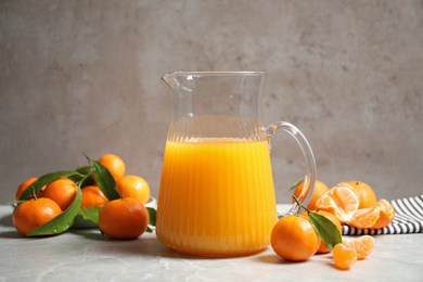 Photo of Jug of fresh tangerine juice and fruits on light table