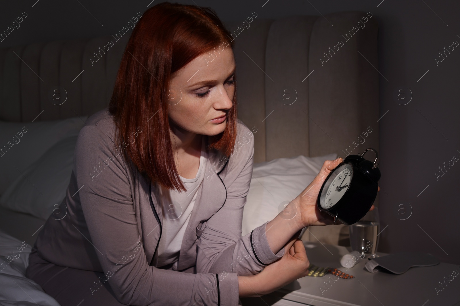 Photo of Woman suffering from insomnia looking at time on alarm clock in bedroom