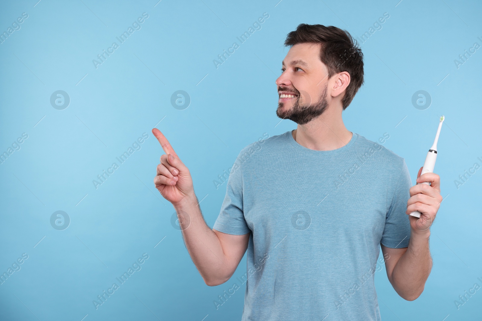 Photo of Happy man holding electric toothbrush on light blue background. Space for text