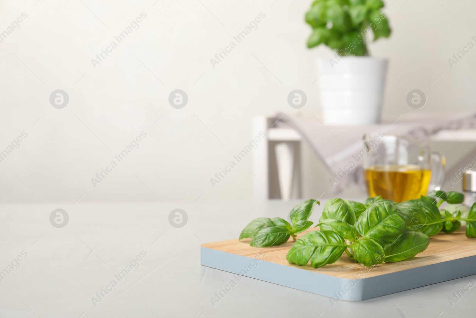 Photo of Wooden board with fresh green basil leaves on table. Space for text