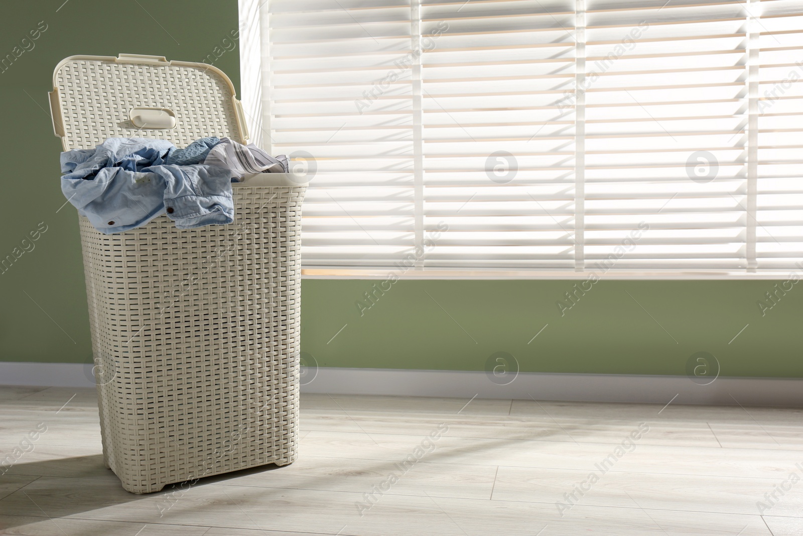 Photo of Laundry basket with clothes near window indoors. Space for text