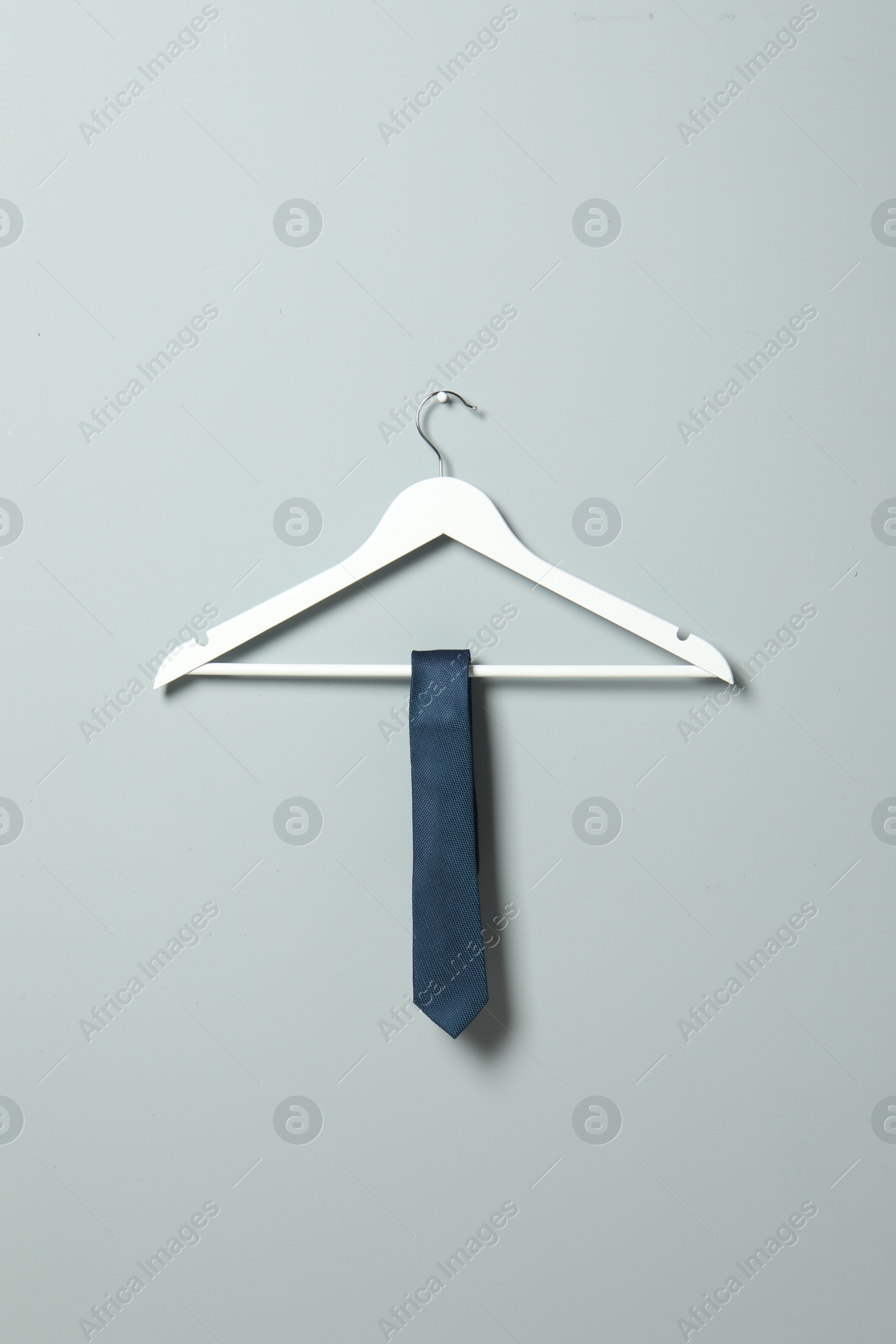 Photo of Hanger with blue necktie on light grey wall