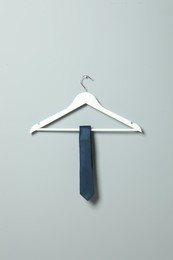 Photo of Hanger with blue necktie on light grey wall