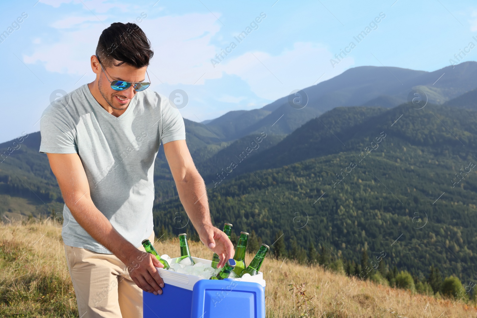 Photo of Man taking bottle of beer from cool box in mountains. Space for text