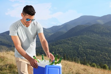 Man taking bottle of beer from cool box in mountains. Space for text